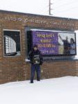 student holds BHC sign in front of Western Illinois University signage