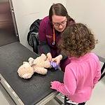 teddy bear being bandaged by vet tech student with child watching