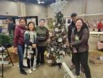 5 people standing with decorated tree at Festival of Trees setup day